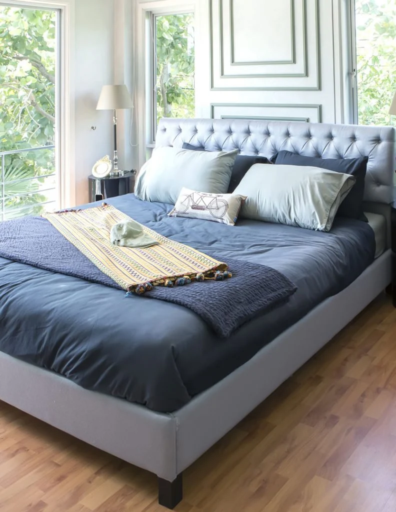 A neatly made navy bed with a grey headboard